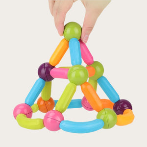 A hand grips a colorful pyramid-shaped toy constructed from magnetic blocks, highlighting its bright hues and engaging form