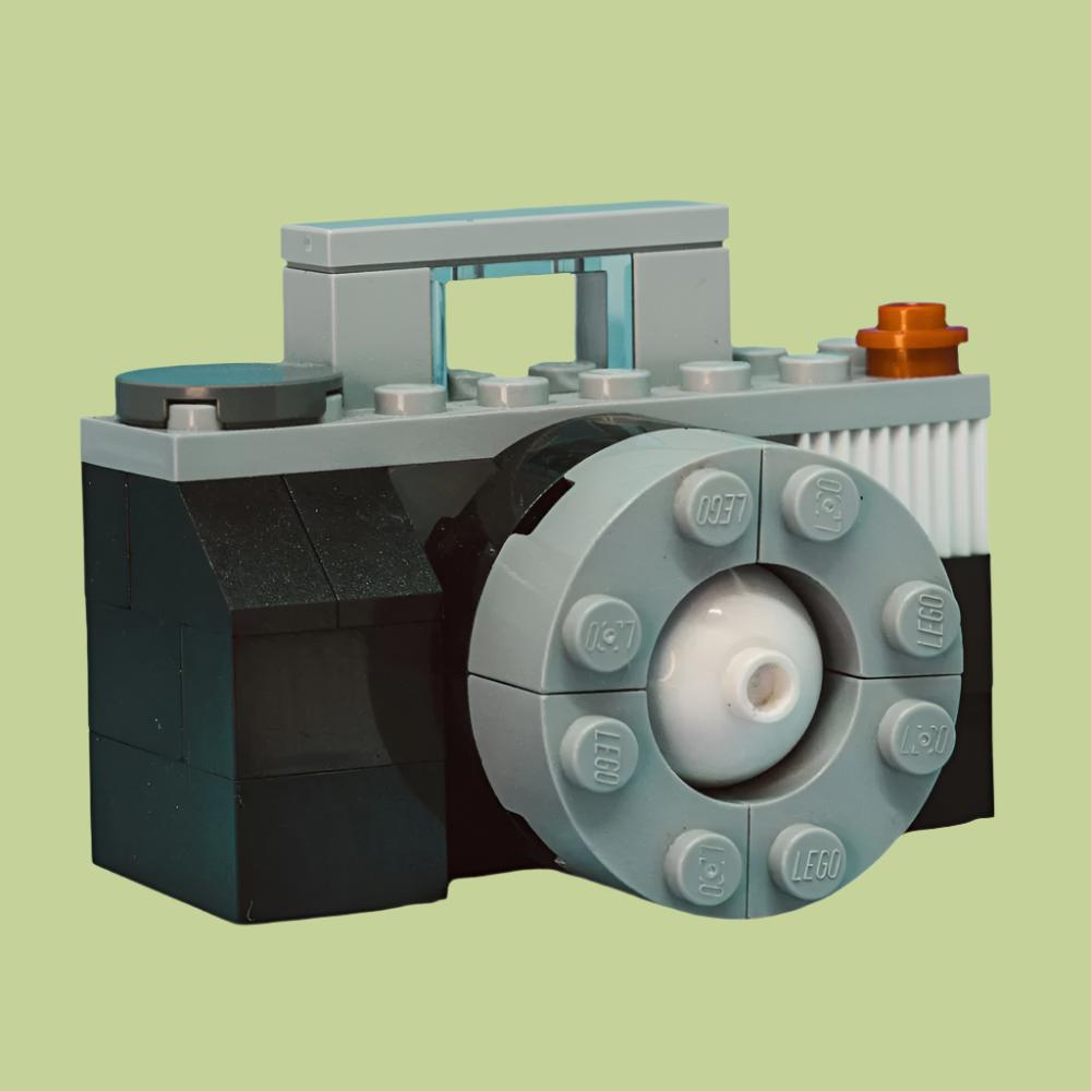 A Lego camera displayed against a vibrant green background, showcasing a playful design made of plastic blocks